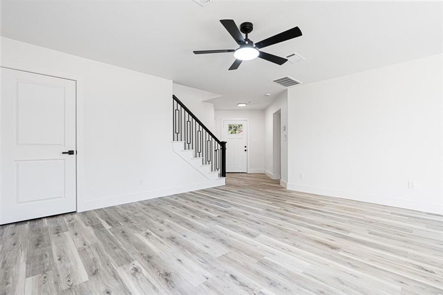 Unfurnished living room with light wood-type flooring, stairs, and ceiling fan