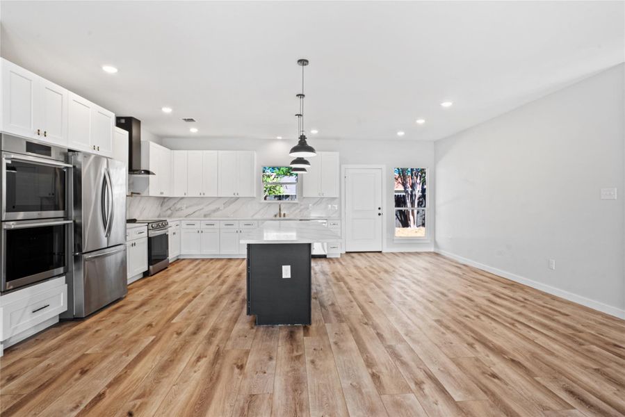 Kitchen featuring white cabinets, appliances with stainless steel finishes, pendant lighting, wall chimney range hood, and a kitchen island