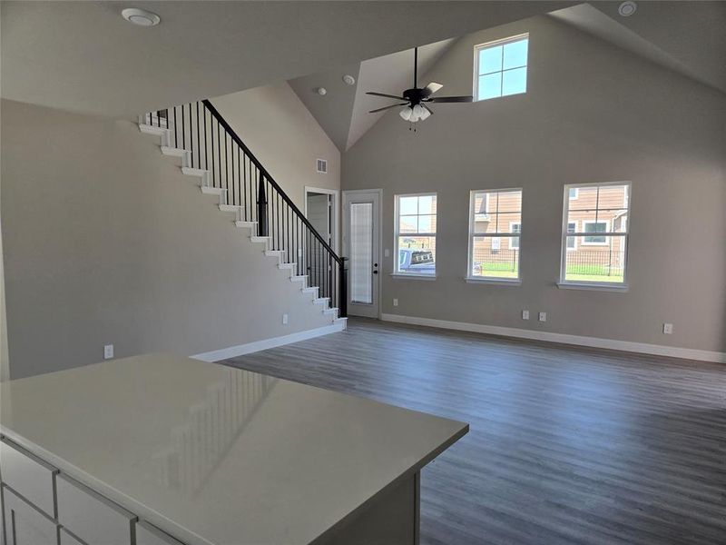 Unfurnished living room featuring high vaulted ceiling, stairway, dark wood-style flooring, and ceiling fan