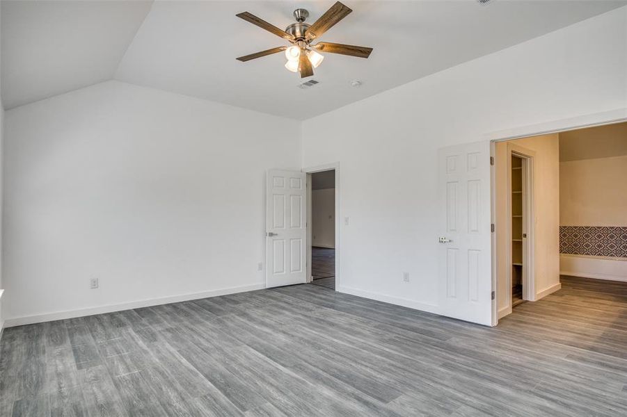 Unfurnished bedroom with ensuite bath, ceiling fan, lofted ceiling, hardwood / wood-style flooring, and a walk in closet Unfurnished bedroom with ensuite bath, ceiling fan, lofted ceiling, hardwood / wood-style flooring, and a walk in closet