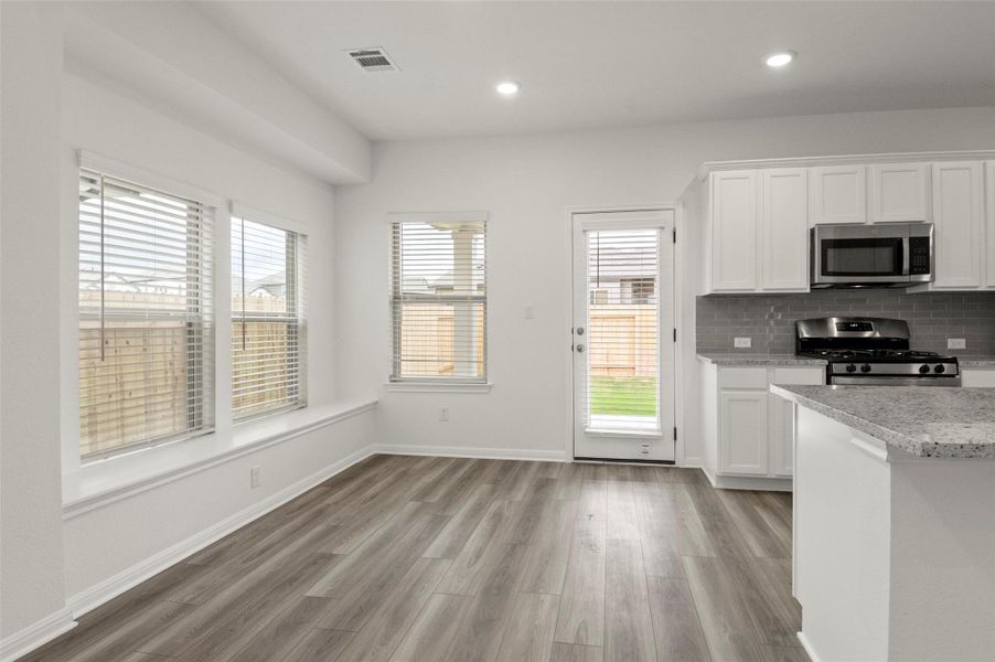 Kitchen featuring stainless steel appliances, white cabinets, decorative backsplash, light wood-style flooring, and recessed lighting