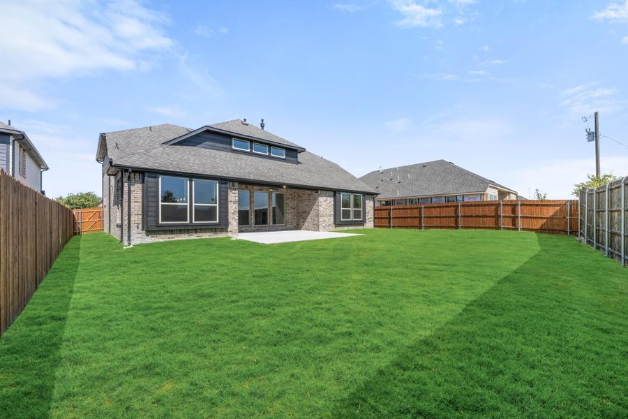 Backyard of brick home with large green lawn, concrete patio, and wood privacy fence Backyard of brick home with large green lawn, concrete patio, and wood privacy fence