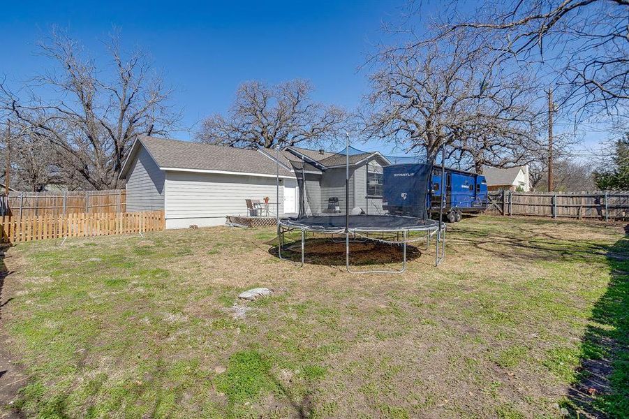 Back of property with a trampoline, a fenced backyard, and a deck