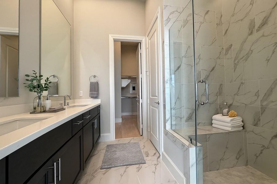 Dual vanities with separate mirrors and frameless glass shower door make this primary bathroom gorgeous.   Decor added virtually.