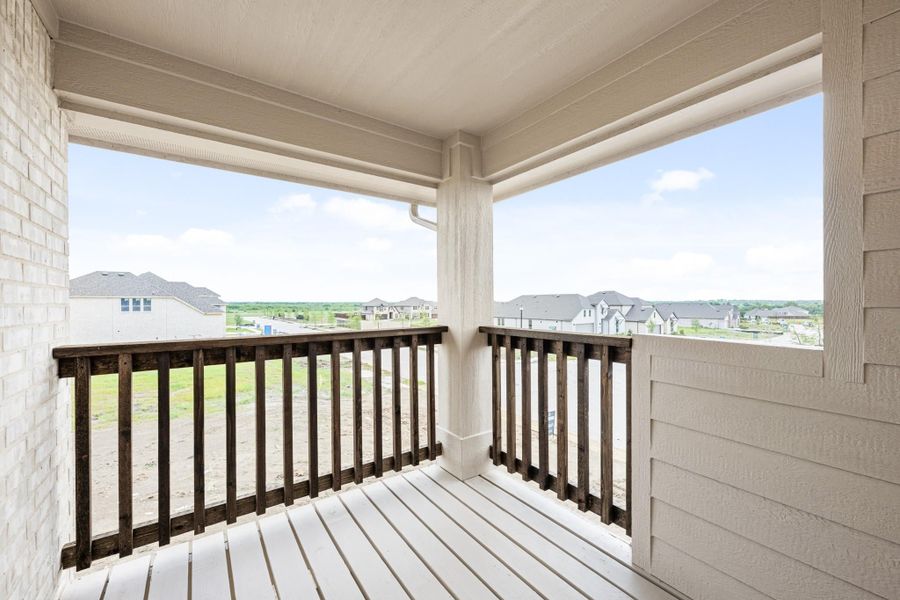 Covered second-floor balcony with dark wood railing and views of neighboring homes and open land
