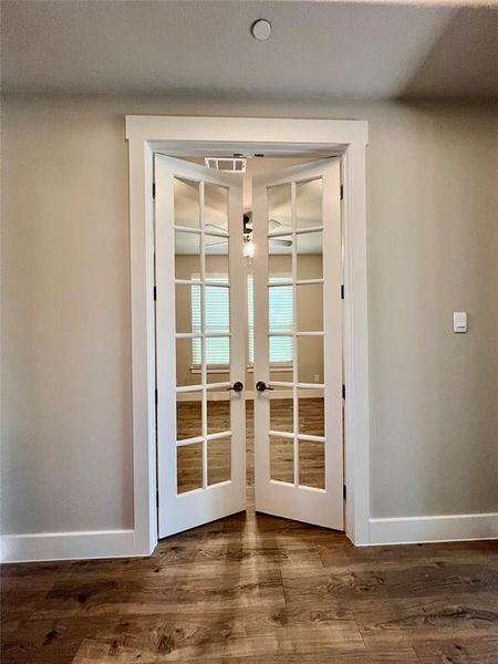 Enclosed office just off the foyer with french doors and dark hardwood / wood-style floors.