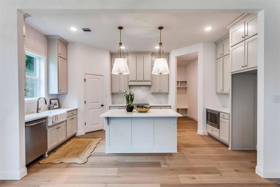 Kitchen featuring a center island, decorative light fixtures, appliances with stainless steel finishes, backsplash, and light wood-style floors