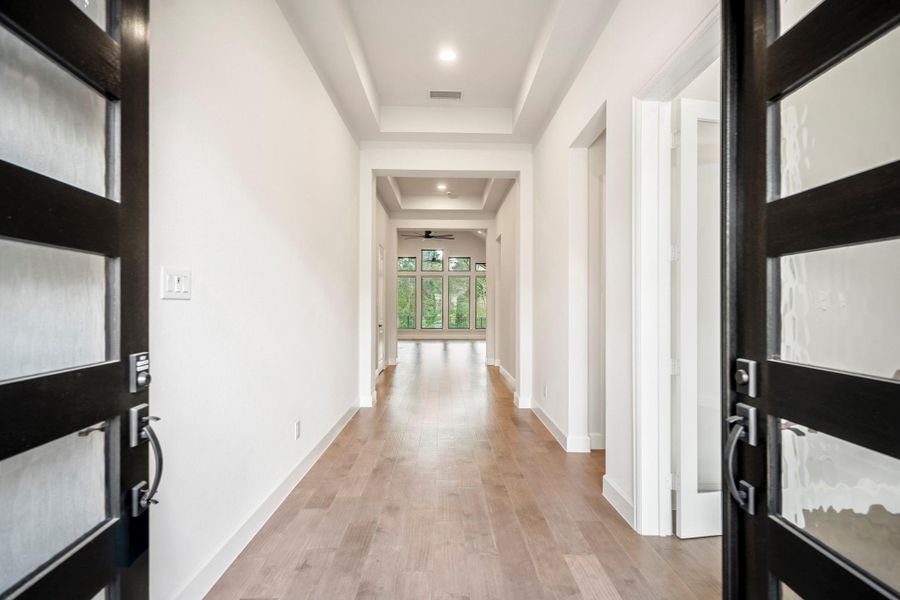 Bright, modern entryway with neutral walls, a tray ceiling, and engineered hardwood flooring. Double doors and a stylish glass-paneled front door enhance the space's elegant and welcoming feel.