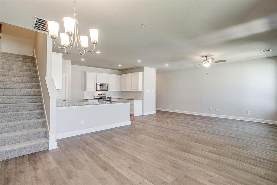 Kitchen with open floor plan, white cabinetry, stainless steel appliances, suspended lighting, and light wood-type flooring