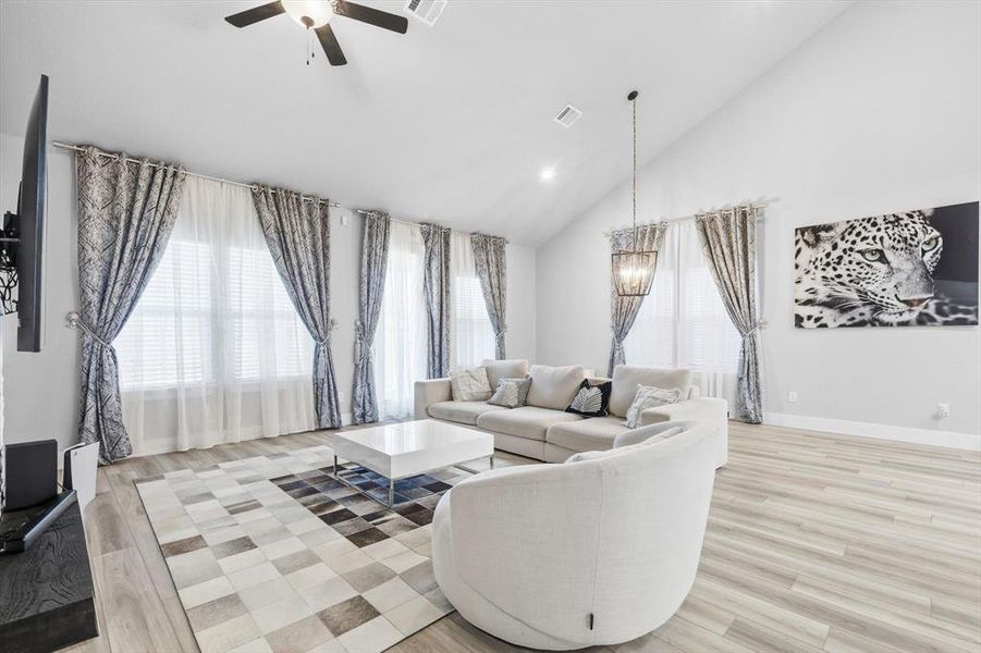 Living area with high vaulted ceiling, light wood finished floors, recessed lighting, a ceiling fan, and a chandelier