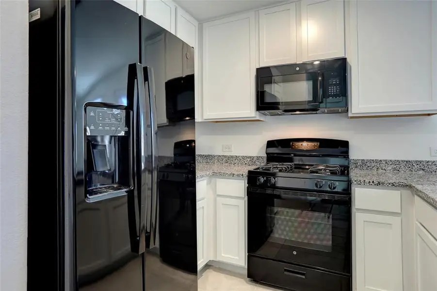 Kitchen with black appliances, white cabinets, light stone counters, and light tile patterned floors