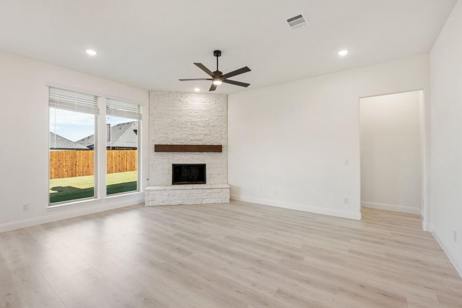 Open living room with light wood floors, white stone fireplace, and ceiling fan Open living room with light wood floors, white stone fireplace, and ceiling fan