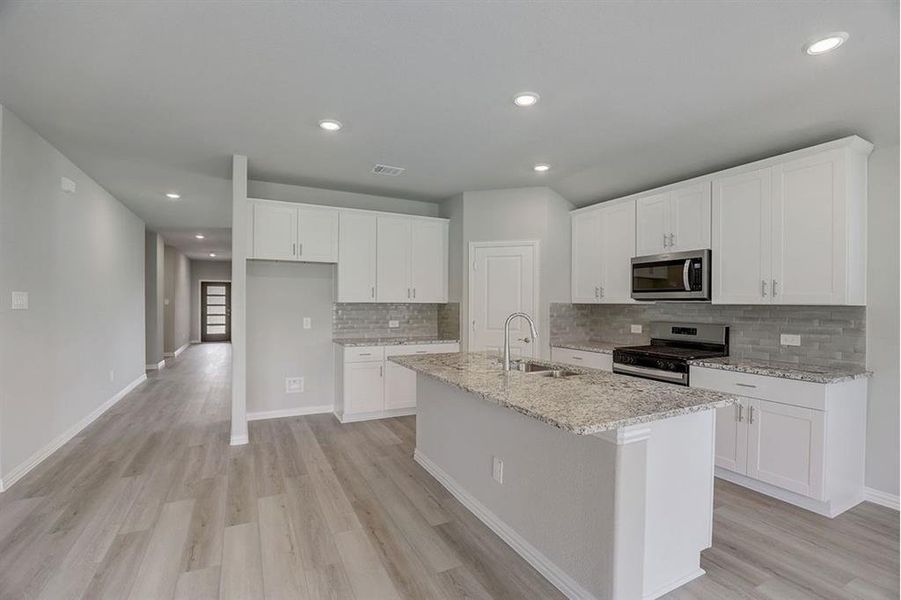 Kitchen with sink, a kitchen island with sink, light hardwood / wood-style flooring, white cabinetry, and appliances with stainless steel finishes