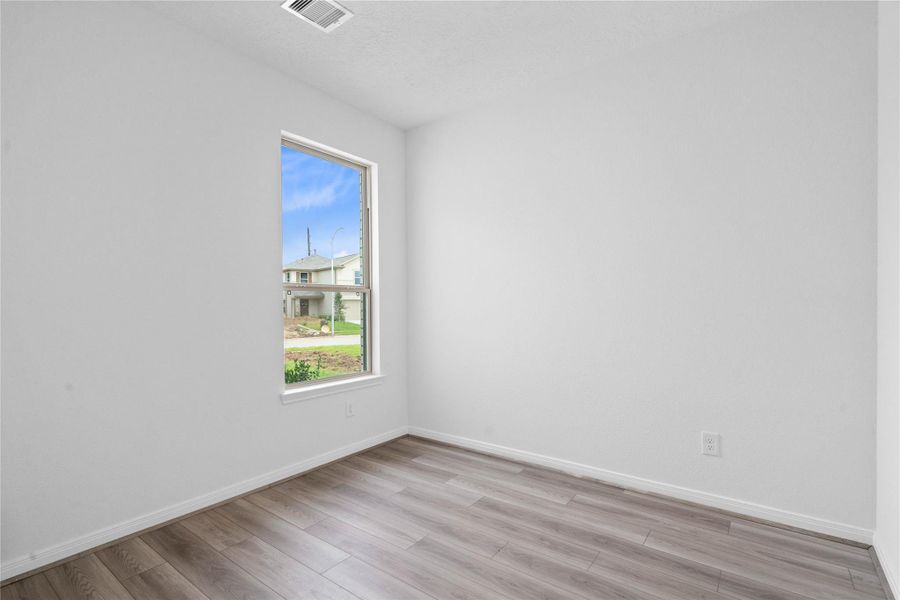 Tucked peacefully in the front of the home, this secondary bedroom offers comfort and style with vinyl plank flooring, neutral paint tones, recessed lighting, a large window, and a generously sized closet