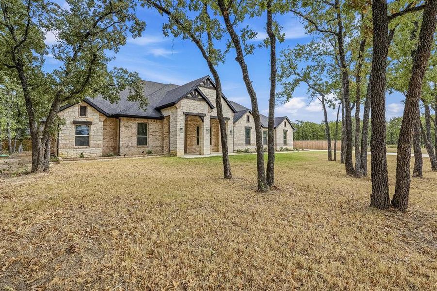 French country inspired facade with stone siding, a shingled roof, a front lawn, and brick siding