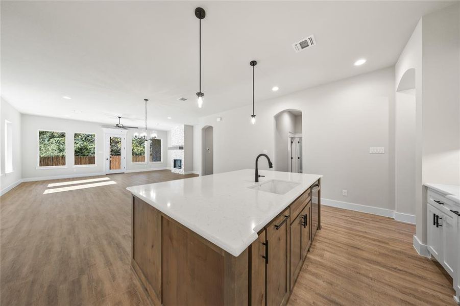 Kitchen featuring open floor plan, light stone countertops, a kitchen island with sink, arched walkways, and light wood-style flooring