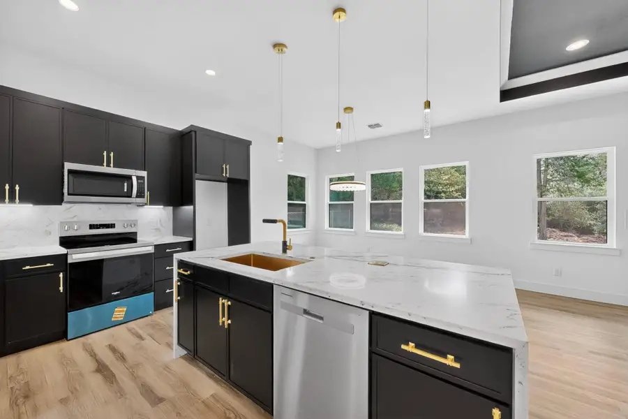A contemporary kitchen features sleek dark cabinetry, white marble-look counters, and a golden sink, all illuminated by pendant lighting.