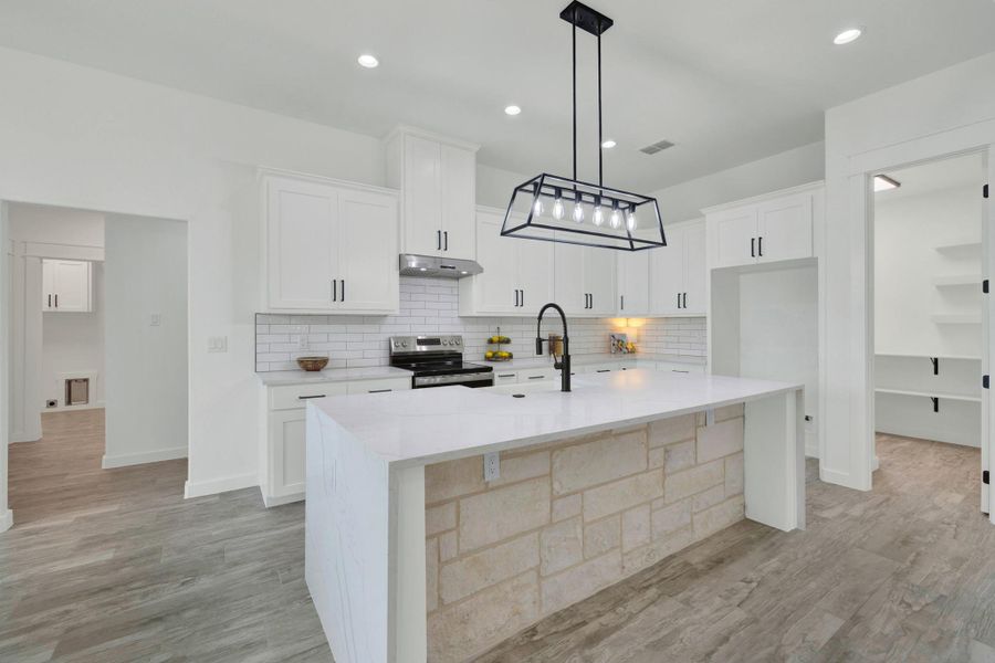 Modern kitchen featuring a stone-clad island with a waterfall countertop, white shaker-style cabinetry, subway tile backsplash, and wood-finish flooring