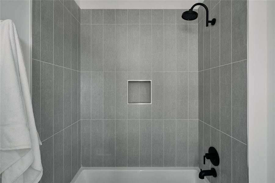 Bathtub shower featuring vertical gray subway tile surround, matte black showerhead, matte black tub filler, and a recessed tiled niche