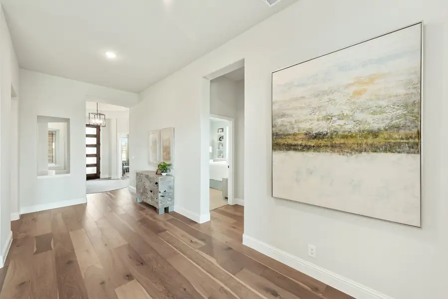 Bright hallway with hardwood floors, white walls, large abstract wall art, and view to front entry with pendant light.