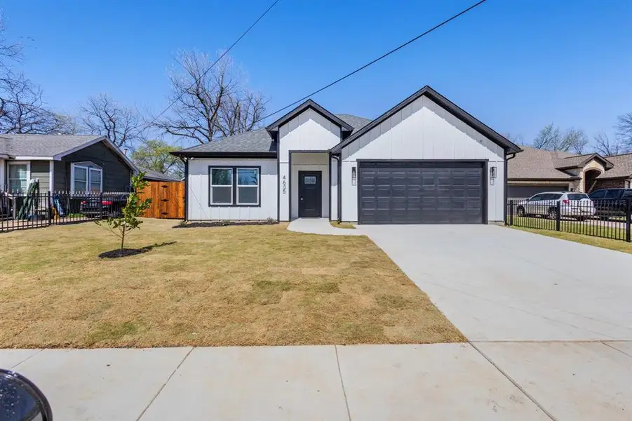 View of front of house featuring an attached garage, concrete driveway, a front yard, and fence