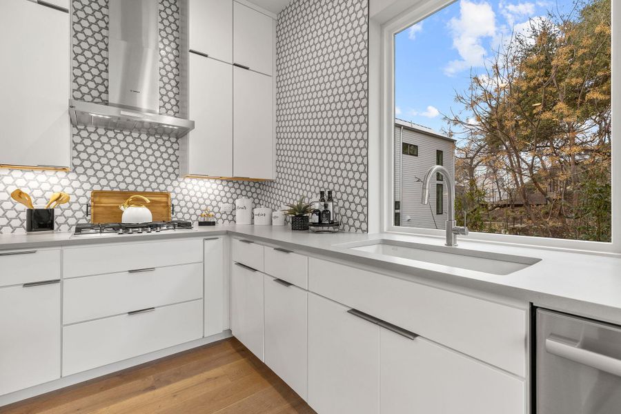 Kitchen with stainless steel appliances, a sink, light countertops, wall chimney range hood, and light wood-type flooring