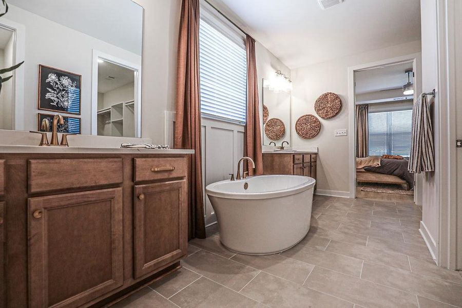 Ensuite bathroom featuring two vanities, plenty of natural light, a freestanding tub, and light tile patterned floors
