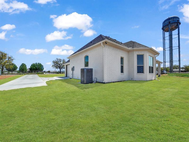View of home's exterior featuring concrete driveway, an attached garage, brick siding, a lawn, and central AC View of home's exterior featuring concrete driveway, an attached garage, brick siding, a lawn, and central AC