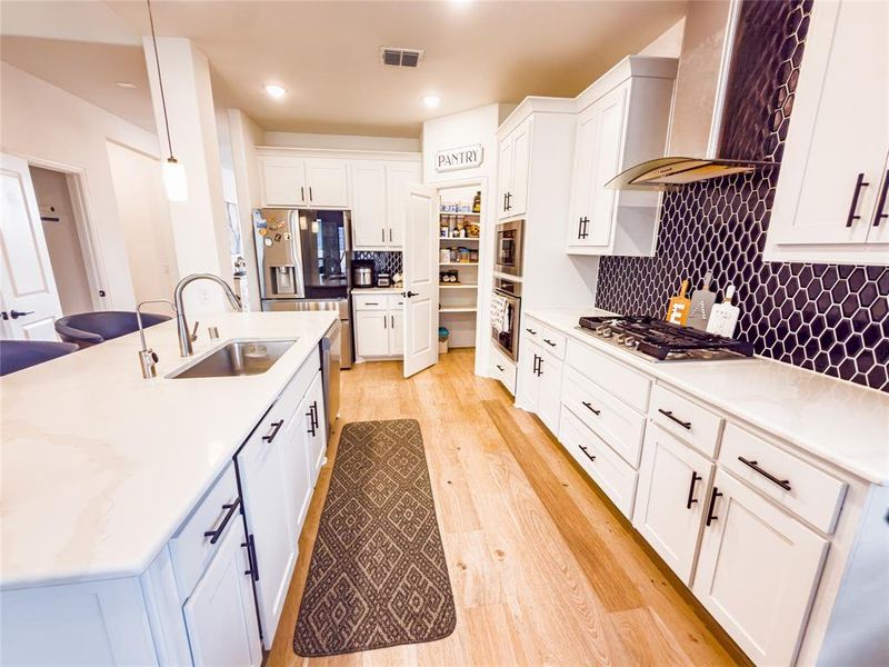 Kitchen featuring white cabinetry, light wood-style flooring, tasteful backsplash, stainless steel appliances, and light stone counters