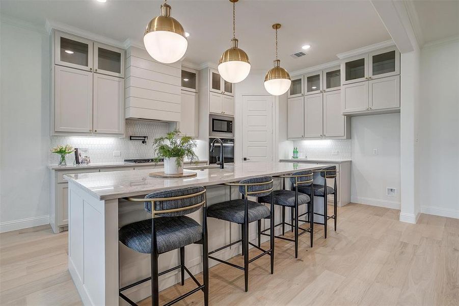 Kitchen featuring custom cabinetry to the ceiling, light hardwood floors, large island with Quartzite countertops, and beautiful hardware.