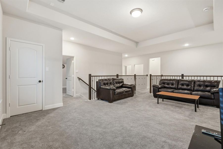 Spacious, carpeted loft area with recessed lighting, featuring a cozy seating arrangement. Neutral walls and trim provide a modern feel, while a railing overlooks the stairs, adding openness to the layout. Spacious, carpeted loft area with recessed lighting, featuring a cozy seating arrangement. Neutral walls and trim provide a modern feel, while a railing overlooks the stairs, adding openness to the layout.
