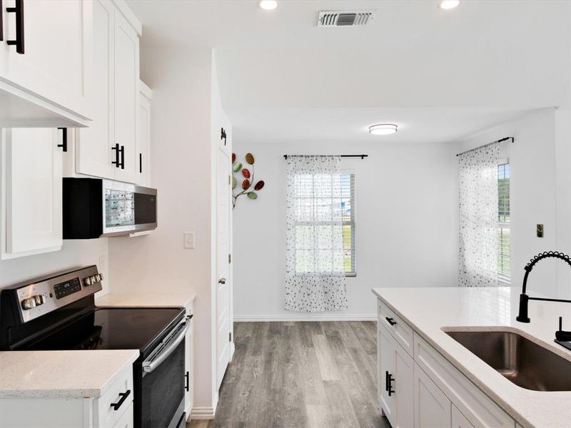 Modern kitchen featuring white shaker cabinetry, stainless steel appliances, light-toned countertops, and dark wood-finish flooring