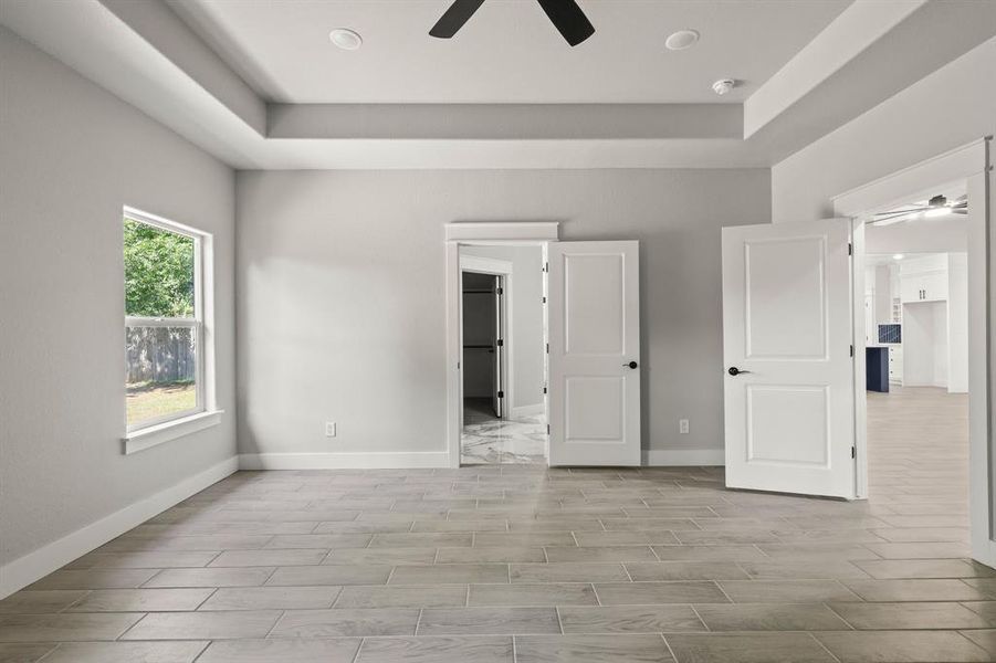 Unfurnished bedroom with a tray ceiling, baseboards, and wood tiled floors