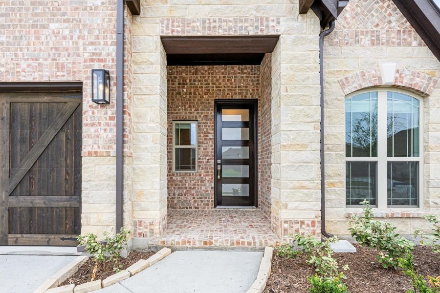 Home entrance with black glass-panel front door, brick and stone exterior, and covered entryway