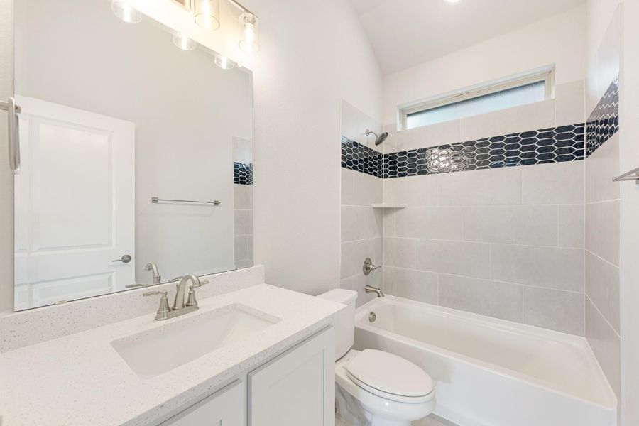 Bathroom with white vanity, quartz countertop, and tiled tub surround with dark accent tile border