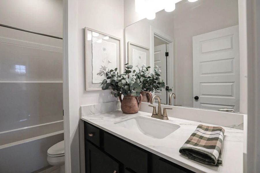 Vanity area featuring a single basin with a gold-tone faucet, stone-look countertop, and dark cabinetry
