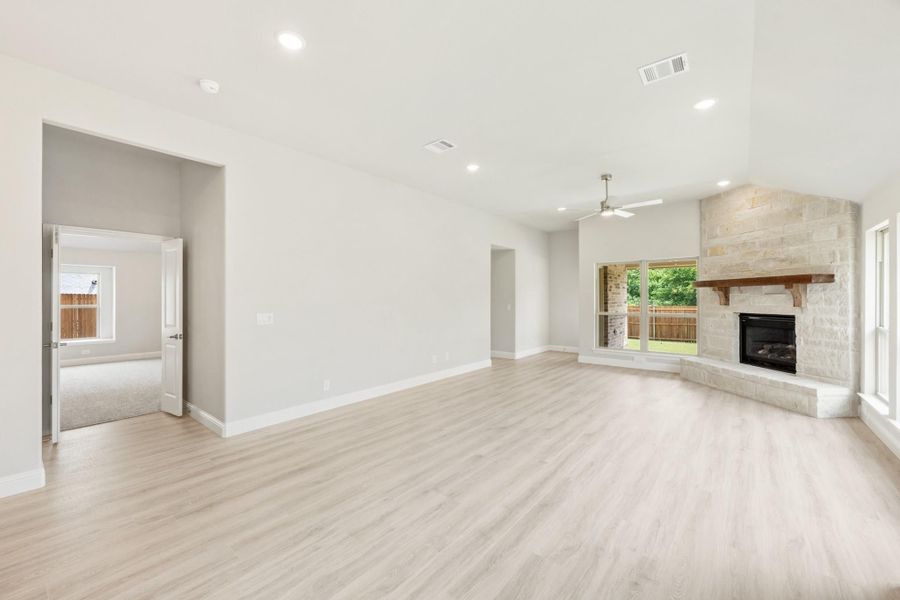 Open living room with light wood floors, stone fireplace, and ceiling fan Open living room with light wood floors, stone fireplace, and ceiling fan