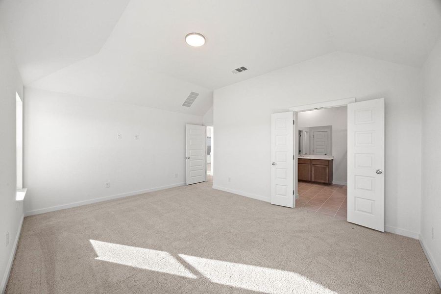 A spacious primary bedroom features soft carpeting, a vaulted ceiling, and an adjoining bathroom.