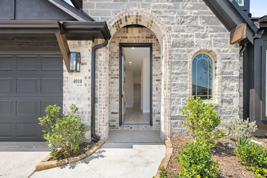 Home entrance with arched brick doorway, stone exterior, and attached garage with landscaping Home entrance with arched brick doorway, stone exterior, and attached garage with landscaping