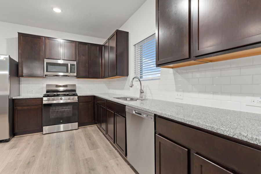 The gourmet kitchen is designed to impress with rich dark cabinetry, gleaming granite countertops, subway tile backsplash, and stainless-steel appliances. Every detail combines elegance and practicality for the perfect culinary space.