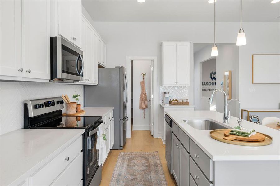 Kitchen with appliances with stainless steel finishes, white cabinetry, light wood-style flooring, tasteful backsplash, and pendant lighting