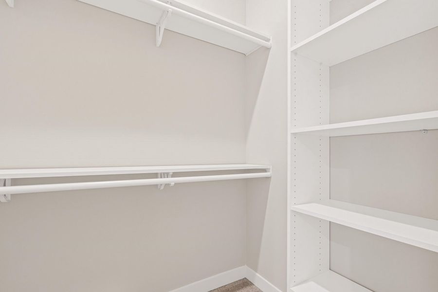 Walk-in closet featuring white wall-mounted shelving, white hanging rods, and light-toned walls Walk-in closet featuring white wall-mounted shelving, white hanging rods, and light-toned walls