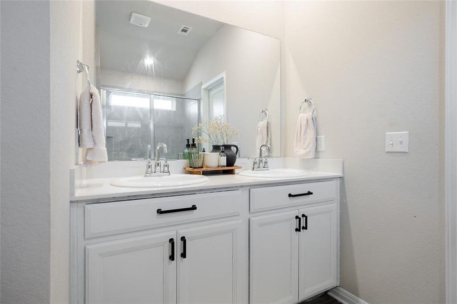 Full bath with double vanity, a stall shower, a textured wall, and lofted ceiling