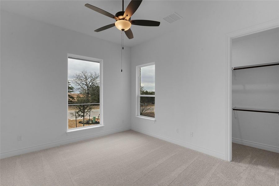 Unfurnished bedroom with a walk in closet, light colored carpet, and a ceiling fan