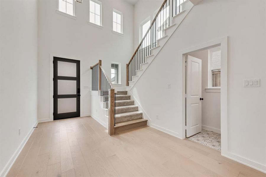 Entryway with healthy amount of natural light, light wood-style flooring, a towering ceiling, and stairway Entryway with healthy amount of natural light, light wood-style flooring, a towering ceiling, and stairway