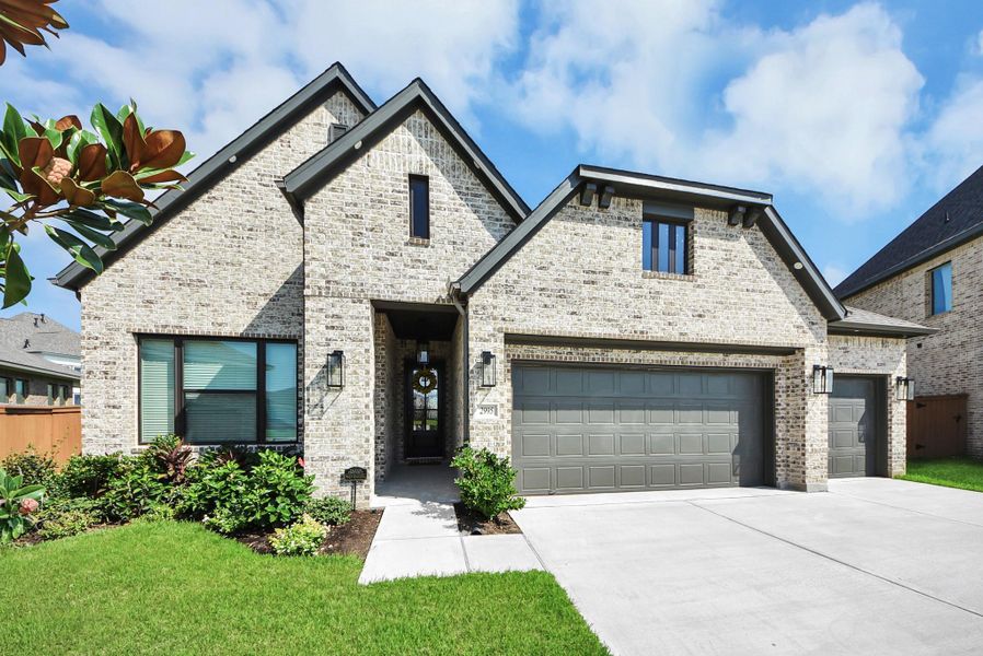 Charming brick home with a modern touch, featuring a spacious three-car garage, lush landscaping, and elegant architectural details.