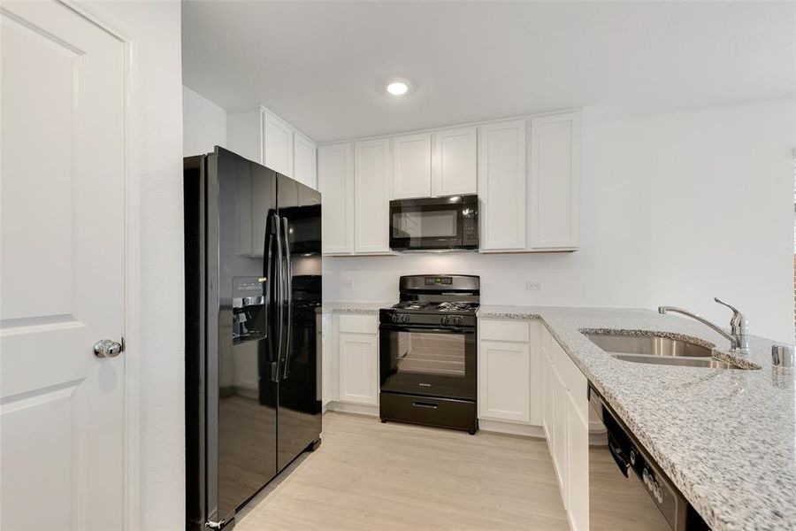 Kitchen with sink, light stone counters, black appliances, white cabinets, and light wood-type flooring