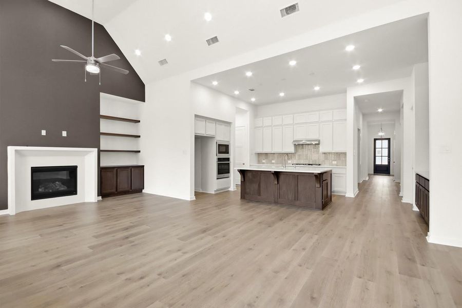Spacious open concept family room flowing seamlessly into the kitchen, highlighted by elevated ceilings, a fireplace, custom built-in cabinetry and shelving, and a bold accent wall that enhances the main living space!