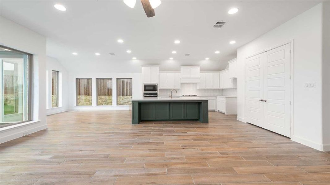 Kitchen with light hardwood / wood-style flooring, decorative backsplash, an island with sink, appliances with stainless steel finishes, and white cabinetry