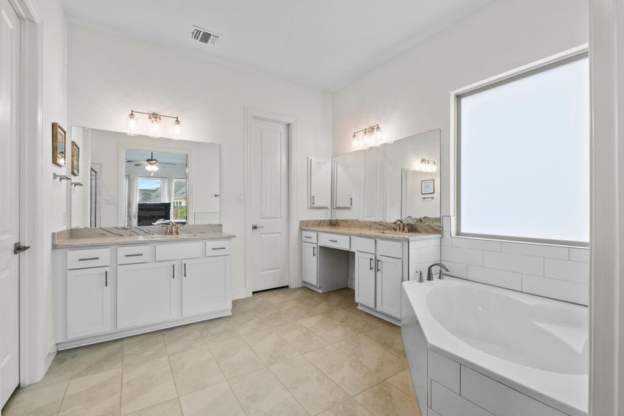 Separate vanities with crisp white cabinetry and brushed nickel hardware provide ample room for morning routines.